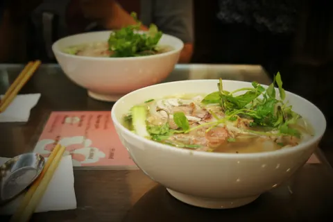 To skåle pho med kød, nudler og friske urter på et bord i Hanoi