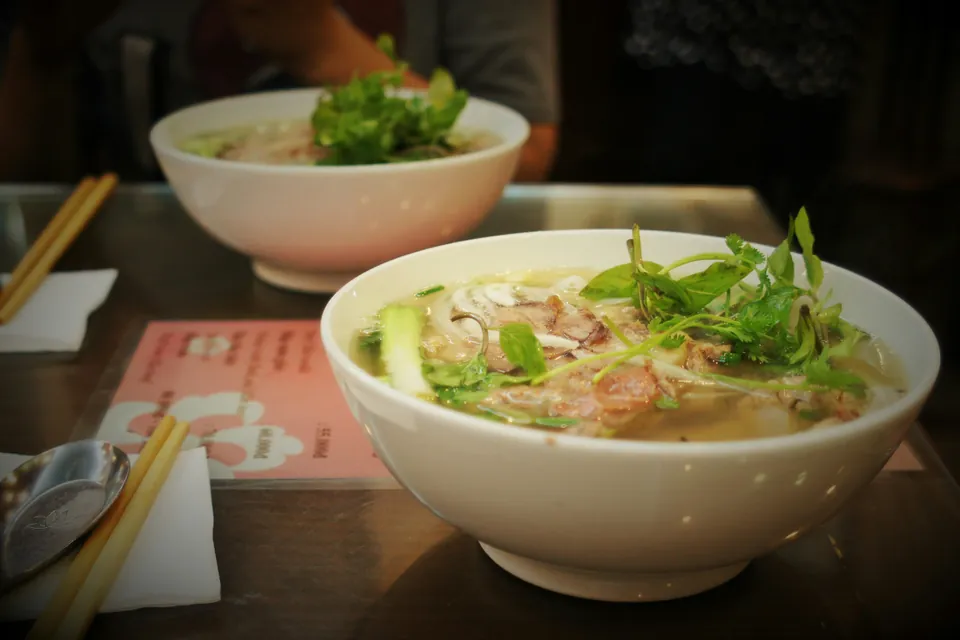 To skåle pho med kød, nudler og friske urter på et bord i Hanoi
